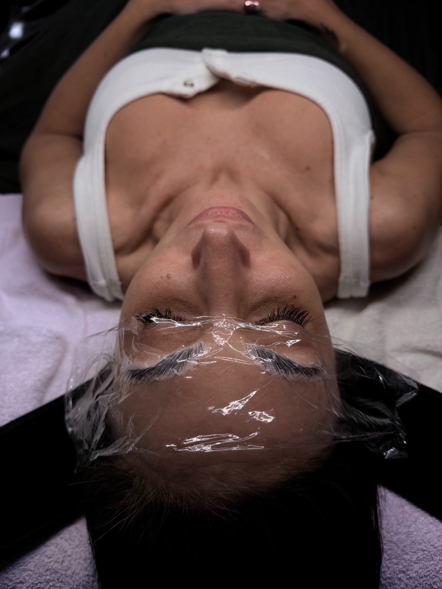 Brow lamination in process — solution on the brows under cling film while the client rests on the bed — The Bronze Lily, St. Petersburg, FL