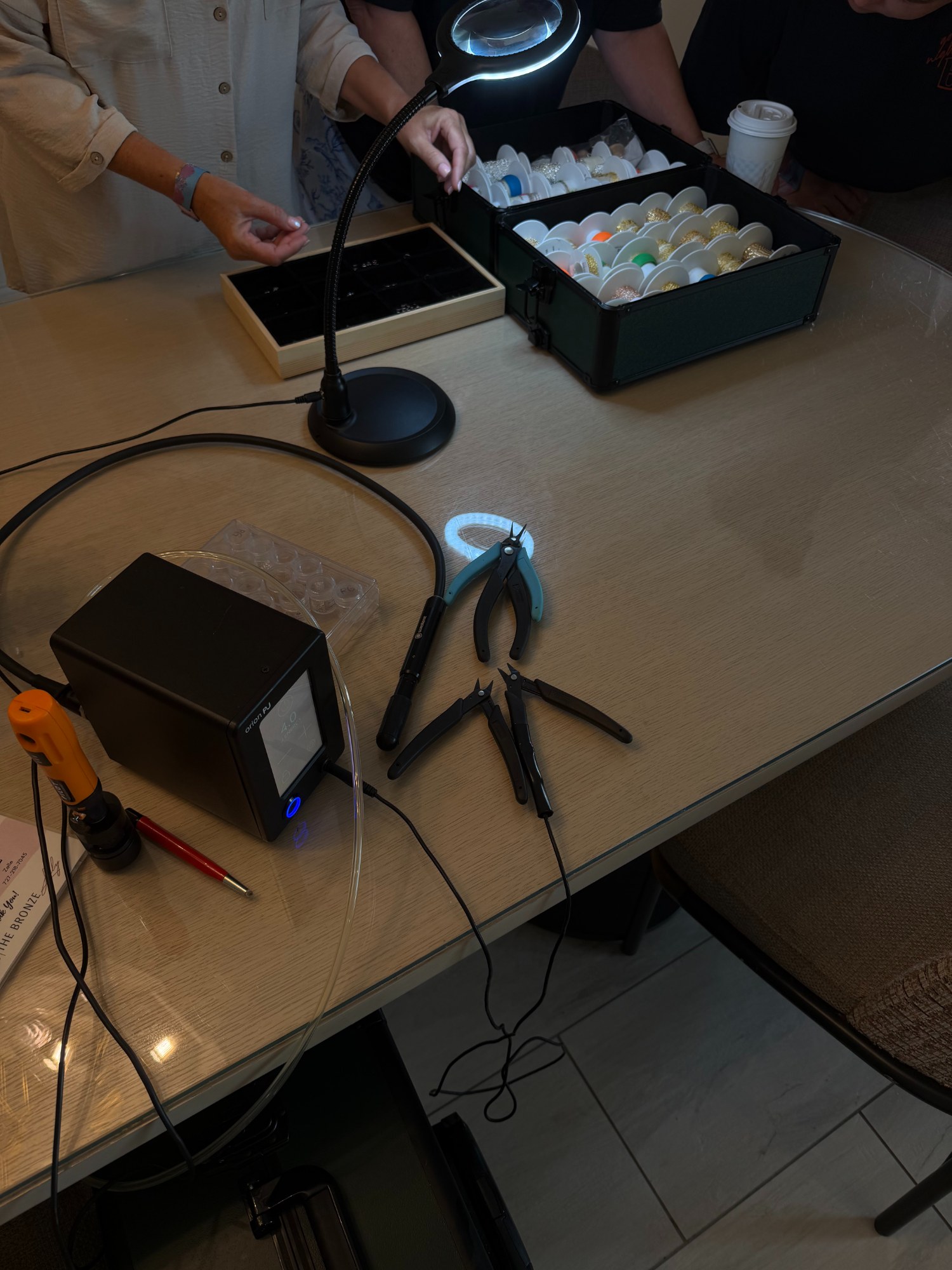 Permanent jewelry welding station set up on a table for a mobile party — welder, chain trays and magnifier lamp — The Bronze Lily, St. Petersburg, FL